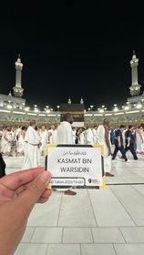 Bukti pelaksanaan badal umroh, kartu jamaah ditunjukkan di depan Ka’bah pada malam hari