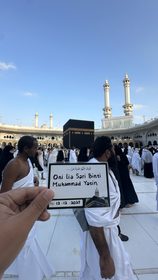 Bukti pelaksanaan badal umroh, kartu jamaah ditunjukkan di depan Ka’bah pada siang hari